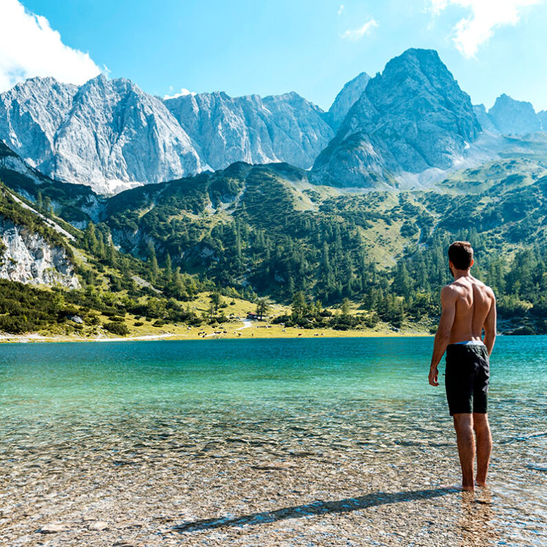 Mann im Wasser am Seeufer, Berge im Hintergrund